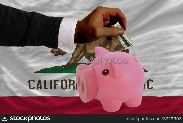 Man putting dollar into piggy rich bank flag of us state of california in foreign currency because of inflation