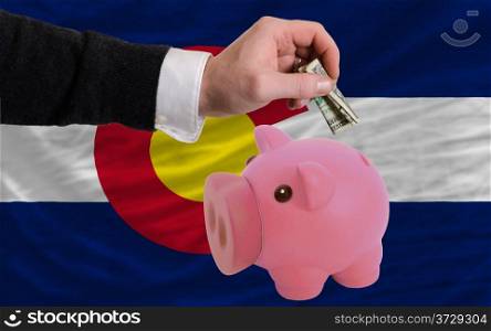 Man putting dollar into piggy rich bank flag of us state of colorado in foreign currency because of inflation