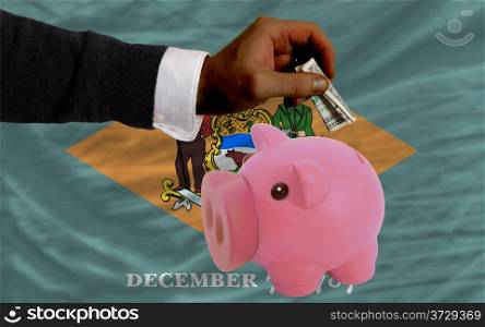 Man putting dollar into piggy rich bank flag of us state of delaware in foreign currency because of inflation