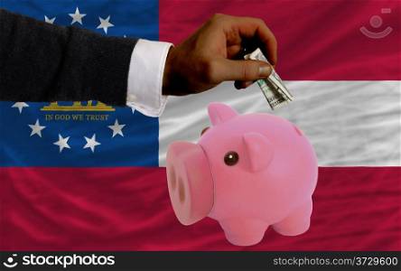 Man putting dollar into piggy rich bank flag of us state of georgia in foreign currency because of inflation