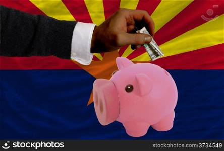Man putting dollar into piggy rich bank flag of us state of arizona in foreign currency because of inflation