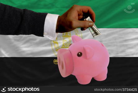 Man putting dollar into piggy rich bank national flag of afghanistan in foreign currency because of inflation