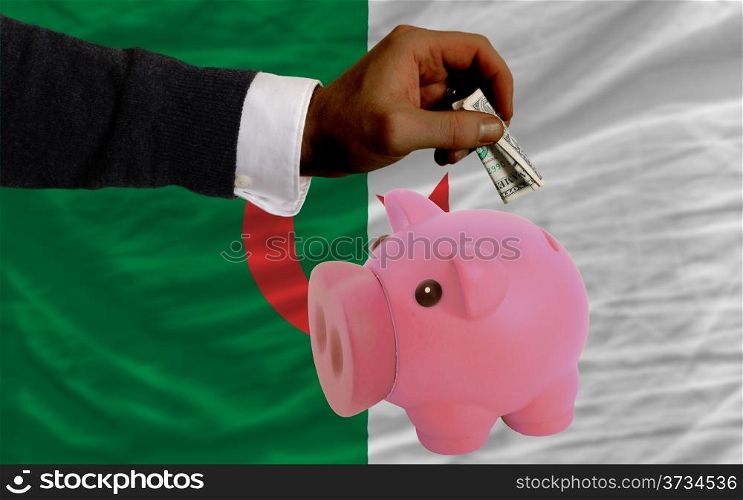Man putting dollar into piggy rich bank national flag of algeria in foreign currency because of inflation