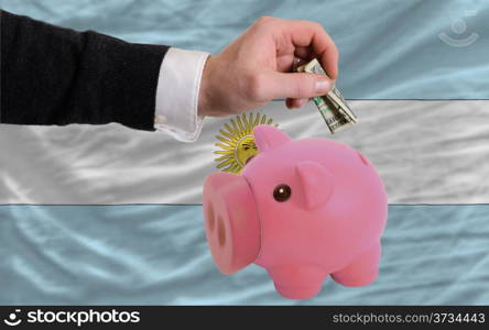 Man putting dollar into piggy rich bank national flag of argentina in foreign currency because of inflation