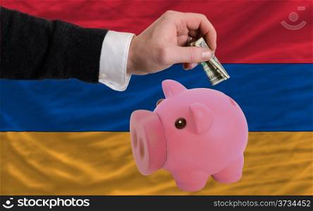 Man putting dollar into piggy rich bank national flag of armenia in foreign currency because of inflation
