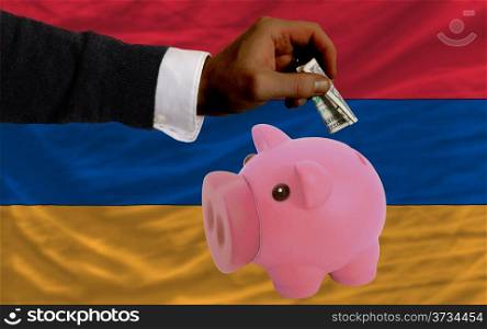 Man putting dollar into piggy rich bank national flag of armenia in foreign currency because of inflation