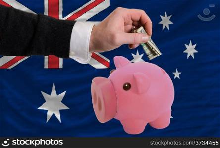 Man putting dollar into piggy rich bank national flag of australia in foreign currency because of inflation