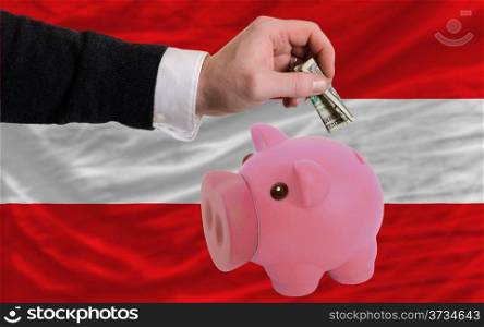 Man putting dollar into piggy rich bank national flag of austria in foreign currency because of inflation