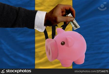 Man putting dollar into piggy rich bank national flag of barbados in foreign currency because of inflation