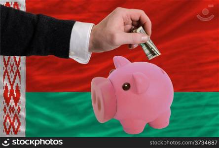 Man putting dollar into piggy rich bank national flag of belarus in foreign currency because of inflation