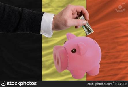 Man putting dollar into piggy rich bank national flag of belgium in foreign currency because of inflation
