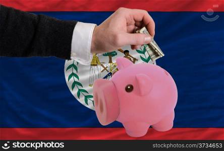 Man putting dollar into piggy rich bank national flag of belize in foreign currency because of inflation