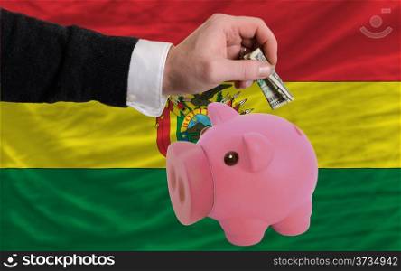 Man putting dollar into piggy rich bank national flag of bolivia in foreign currency because of inflation