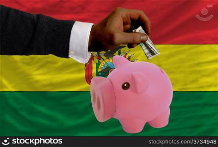 Man putting dollar into piggy rich bank national flag of bolivia in foreign currency because of inflation