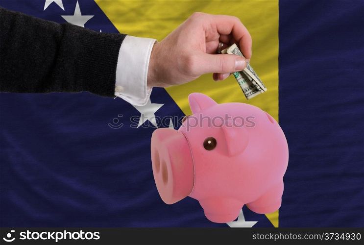 Man putting dollar into piggy rich bank national flag of bosnia herzegovina in foreign currency because of inflation