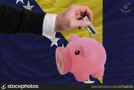 Man putting dollar into piggy rich bank national flag of bosnia herzegovina in foreign currency because of inflation