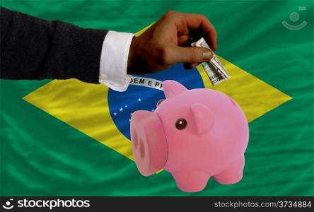Man putting dollar into piggy rich bank national flag of brazil in foreign currency because of inflation