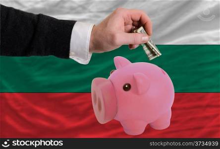 Man putting dollar into piggy rich bank national flag of bulgaria in foreign currency because of inflation