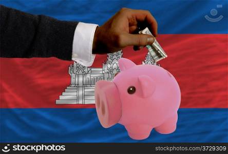 Man putting dollar into piggy rich bank national flag of cambodia in foreign currency because of inflation