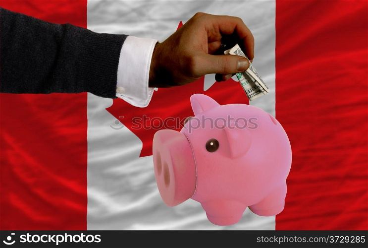 Man putting dollar into piggy rich bank national flag of canada in foreign currency because of inflation