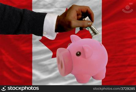 Man putting dollar into piggy rich bank national flag of canada in foreign currency because of inflation
