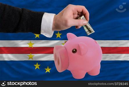 Man putting dollar into piggy rich bank national flag of cape verde in foreign currency because of inflation