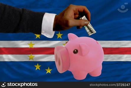 Man putting dollar into piggy rich bank national flag of cape verde in foreign currency because of inflation