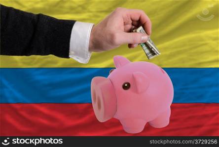 Man putting dollar into piggy rich bank national flag of columbia in foreign currency because of inflation