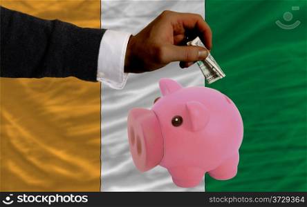 Man putting dollar into piggy rich bank national flag of cote ivore in foreign currency because of inflation