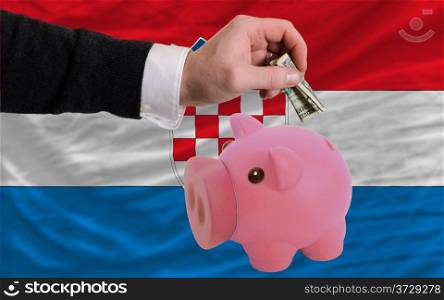 Man putting dollar into piggy rich bank national flag of croatia in foreign currency because of inflation