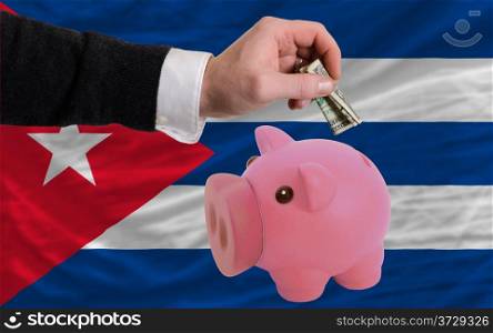 Man putting dollar into piggy rich bank national flag of cuba in foreign currency because of inflation
