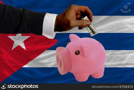 Man putting dollar into piggy rich bank national flag of cuba in foreign currency because of inflation