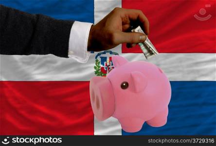 Man putting dollar into piggy rich bank national flag of dominican in foreign currency because of inflation