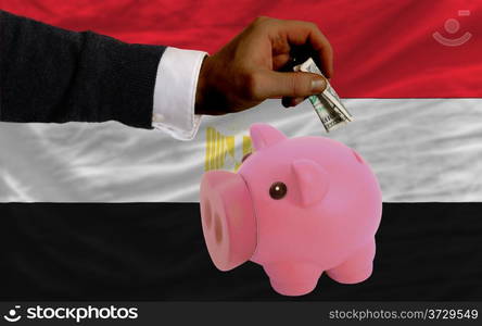 Man putting dollar into piggy rich bank national flag of egypt in foreign currency because of inflation