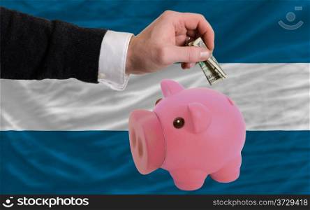Man putting dollar into piggy rich bank national flag of el salvador in foreign currency because of inflation