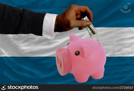 Man putting dollar into piggy rich bank national flag of el salvador in foreign currency because of inflation