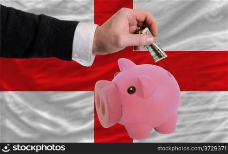 Man putting dollar into piggy rich bank national flag of england in foreign currency because of inflation