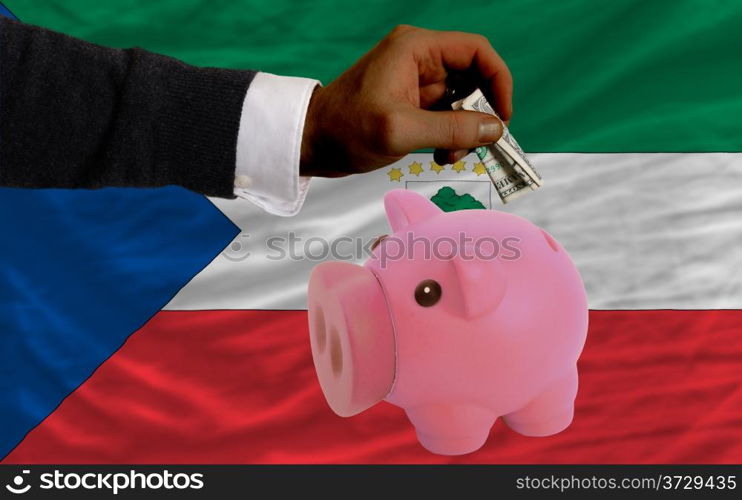 Man putting dollar into piggy rich bank national flag of equatorial guinea in foreign currency because of inflation