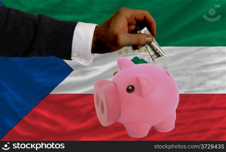 Man putting dollar into piggy rich bank national flag of equatorial guinea in foreign currency because of inflation