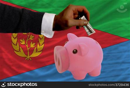 Man putting dollar into piggy rich bank national flag of eritrea in foreign currency because of inflation
