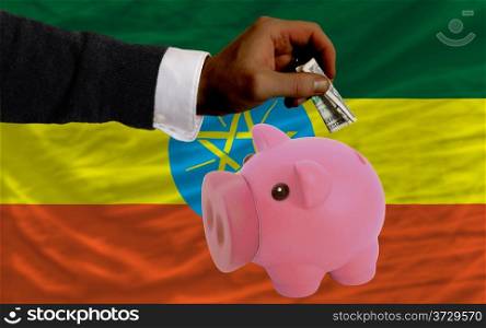 Man putting dollar into piggy rich bank national flag of ethiopia in foreign currency because of inflation
