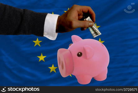 Man putting dollar into piggy rich bank national flag of europe in foreign currency because of inflation