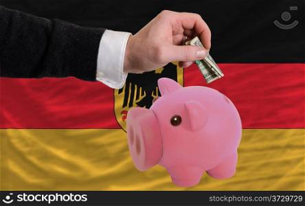 Man putting dollar into piggy rich bank national flag of germany in foreign currency because of inflation