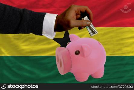 Man putting dollar into piggy rich bank national flag of ghana in foreign currency because of inflation