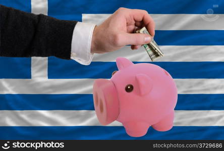 Man putting dollar into piggy rich bank national flag of greece in foreign currency because of inflation