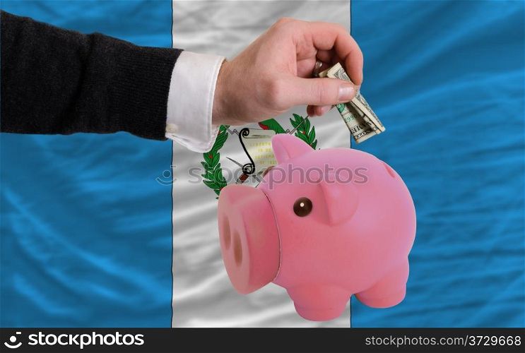 Man putting dollar into piggy rich bank national flag of guatemala in foreign currency because of inflation
