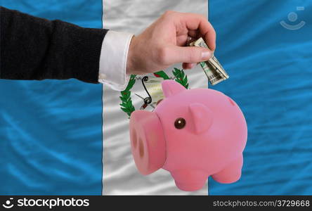 Man putting dollar into piggy rich bank national flag of guatemala in foreign currency because of inflation