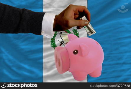 Man putting dollar into piggy rich bank national flag of guatemala in foreign currency because of inflation