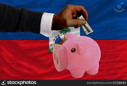 Man putting dollar into piggy rich bank national flag of haiti in foreign currency because of inflation