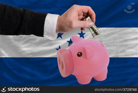 Man putting dollar into piggy rich bank national flag of honduras in foreign currency because of inflation